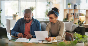 Couple reviewing finances at home with a calculator and paperwork while planning how to budget their income